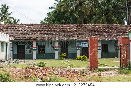 Chikunda India - October 28 2013: The pastel painted Muslim primary school of the village features a tiled saddle roof and messages in Urdu Arabic and Kannada language. Indian national flag on pillars. Green vegetation.