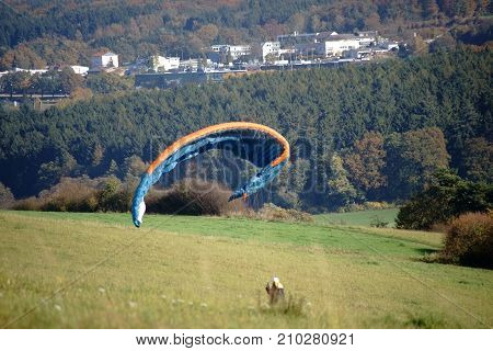 A paraglider is standing on a hill and straightens its paraglider.