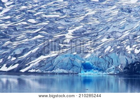 Vast Snow Topped Glacier with Bright Turquoise Ice From Recent Calving and Reflection in Ocean