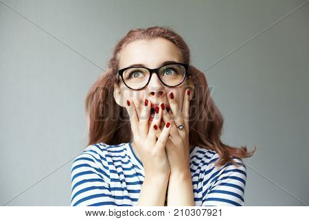 Oh my god. Fascinated emotional cute young woman with red nails and two ponytails exclaiming in astonishment and covering her mouth feeling happy and excited about being accepted to college