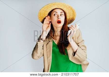 a funny girl in a green blouse and a big hat is holding a mobile phone and listening to extraneous sounds