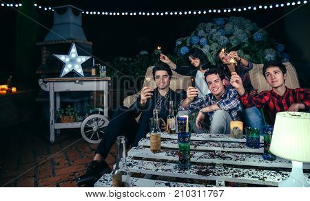 Happy young friends holding sparklers and having fun in a outdoors night party. Friendship and celebrations concept.