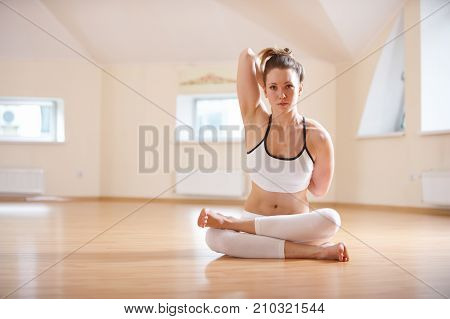 Beautiful woman practices yoga asana Gomukhasana - Cow face pose in the yoga studio.