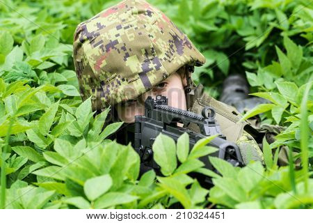 Portrait of armed woman with camouflage. Young female soldier observe with firearm. Child soldier with gun in war green goutweed background. Military army people concept