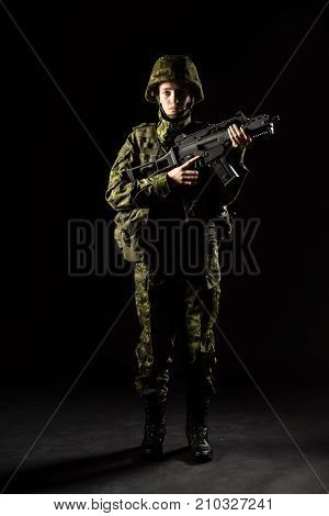 Portrait of armed woman with camouflage. Young female soldier observe with firearm. Child soldier with gun in war black background. Military army people concept