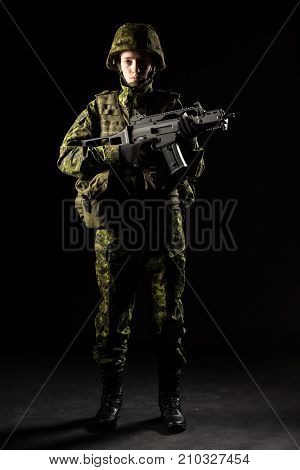 Portrait of armed woman with camouflage. Young female soldier observe with firearm. Child soldier with gun in war black background. Military army people concept