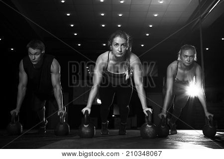 Group of muscular fit people exercising with kettlebells in gym. Push up exercise. Strength or powerlifting training. Fitness, sports concept.