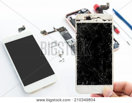 Close-up of cracked smartphone screen in technician hand on blurred smartphone component background