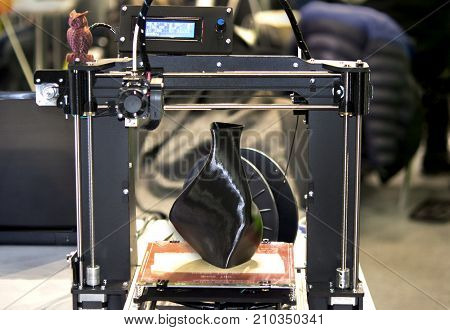 3D printer printing a model in the form of black vase close-up. The concept modern additive technology. The 4ht industrial revolution.