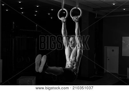 Muscular young man doing intense workout on gymnastics rings. Strength or callistenics workout. Fitness, sports concept.