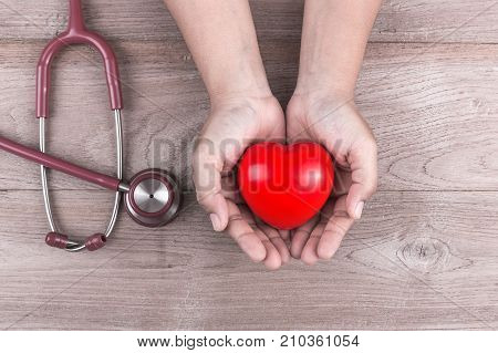 Check Heart Concept : Woman Hands Holding Red Heart And Stethoscope On Brown Wooden Table