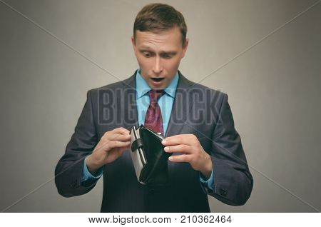Young business man in a suit holds an empty wallet in his hand and looks for money in it. Pay the debt. Bankruptcy concept.