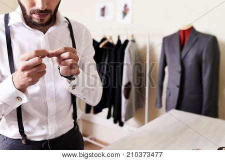 Mid section portrait of handsome young man trying to put thread through needle in modern atelier workshop, copy space