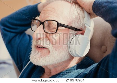 Time for meditation. Handsome elderly man keeping smile on his face and closing eyes while listening music