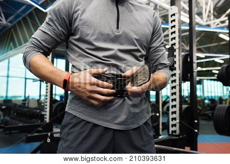 Mid section of modern sportsman putting on back protective belt for work out in modern gym