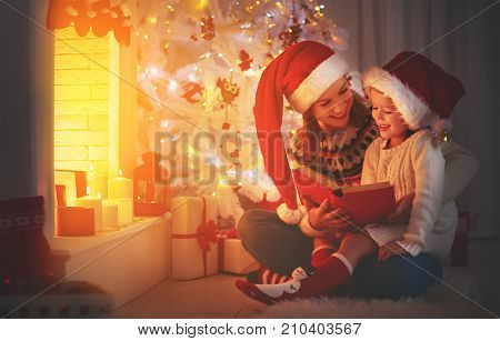 Christmas Eve. family mother and child daughter reading magic book at home near the fireplace and Christmas tree