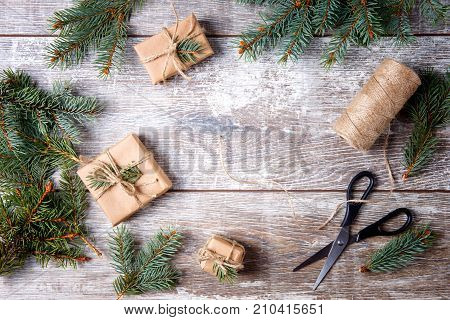 Christmas gifts on a wooden background. Scissors, threads, spruce branches. View from above. Concept of holidays.