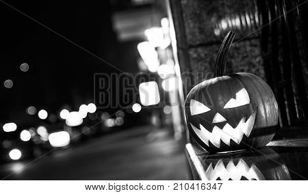 BLACK WHITE concept of Halloween. Pumpkin with a face stands on the street and decorates the street scaring passers-by people.