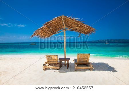 Relaxing couch chairs with straw parasol on Puka sandy beach at Boracay island. Philippines.