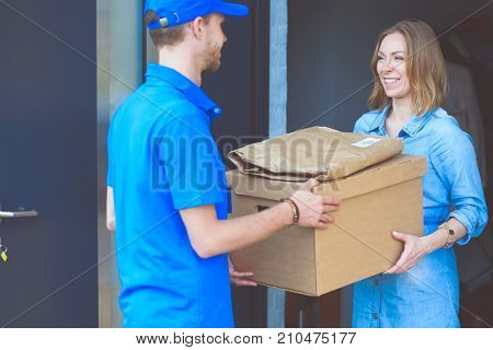 Smiling delivery man in blue uniform delivering parcel box to recipient - courier service concept. Smiling delivery man in blue uniform