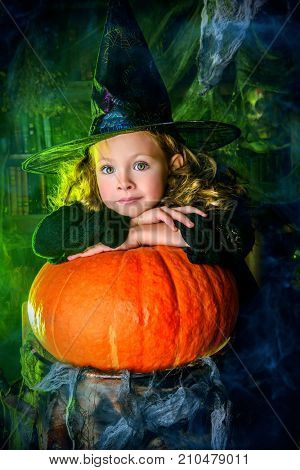 Happy Halloween. Cute child girl in witch costume is in a witch's lair with pumpkin. 