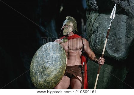 Roman legionary walking in the dark forest with his shield and a spear.