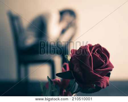 Retro sad woman sitting and crying with red rose in focus. Lonly love emotion concept.