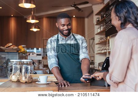 Customer paying a smiling barista for a purchase in a cafe using a smartphone and nfs technology