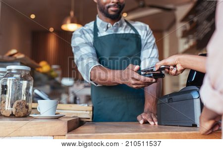 Closeup of a barista using nfs technology to help a customer pay for a purchase with their smartphone in a cafe