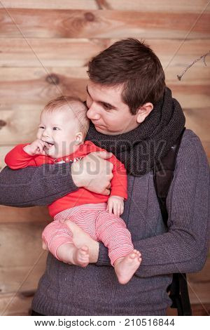 Young father holding son against wooden background. Vertical shot