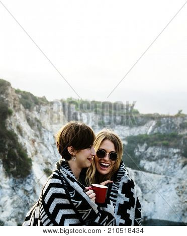 Girlfriends cuddle together under blanket on top of the mountain