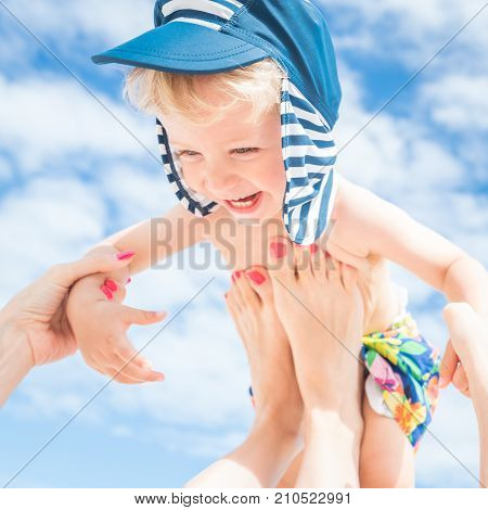 Mom throws up her smiling baby boy in the blue skysummer time.