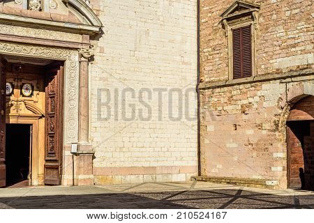 A corner of a square in the town of Spello with the main entrrance of the cathedral and a residential building with a shadow of a man.