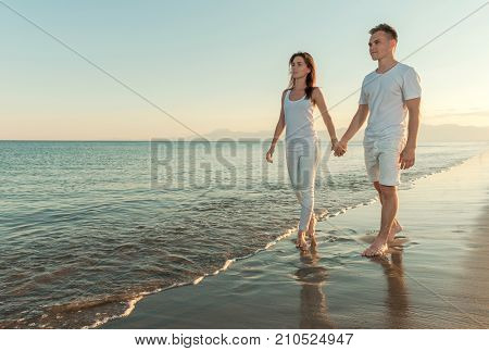 young couple holding hands while walking along the beach