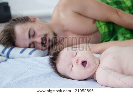 sleeping parent and baby waking up yawning in the morning lying on bed together happy family