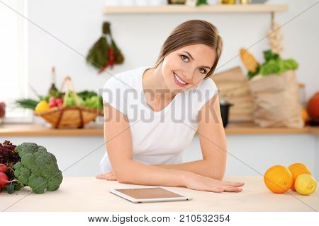 Young woman is making online shopping by tablet computer and credit card. Housewife found new recipe for cooking in a kitchen.