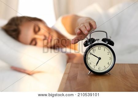 Sleepy young woman stretching hand to ringing alarm willing turn it off. Early wake up, not getting enough sleep, getting work concept