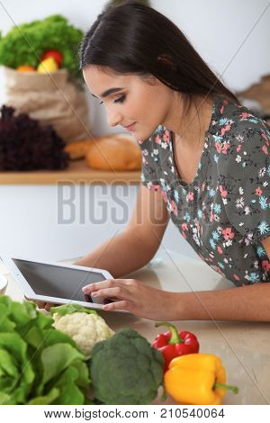 Young hispanic woman is making online shopping by tablet computer and credit card. Housewife found new recipe for cooking in a kitchen.