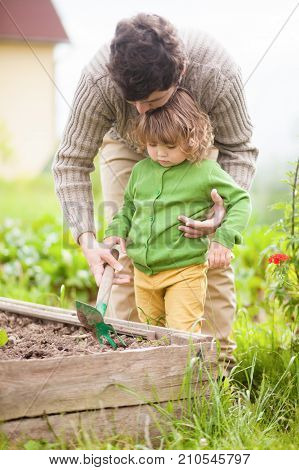 Father and child cutivating ground in garden bad in spring. Family having fun. Active leisure.