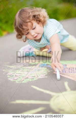 Sunny and warm summer days and happy chilhood. Cute little girl drawing with chalk crayons outdoors.