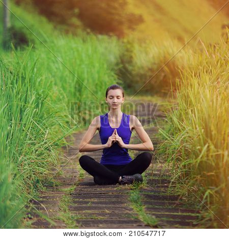Young Slim Woman In Tight Sportswear With Dark Hair Practicing Yoga Outdoors Among Green Grass Summe