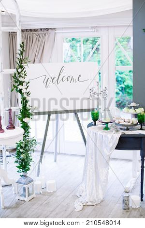 Wedding decorations with flowers in Boho style with macarons on a table with large number od various decorations. Large windows on background. DIY