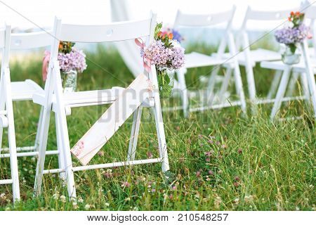 Beautifully decorated white chairs for wedding reception outdoors. Wedding decor. Close up shot. Details. Floral