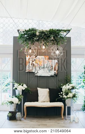 Wedding decorations with flowers in Boho style with sofa in front of big windows on background. Stylish interior DIY. Metalic details.