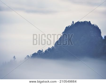 View Into Misty Valley. High Trees And Rocky Peaks Increased From Thick Fog.  The First Sun Rays