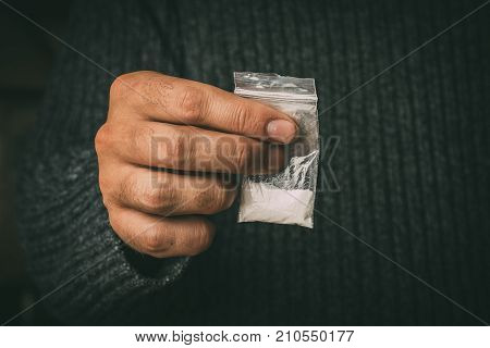Male hand holds packet with white narcotic - cocaine, meth or another drug, toned