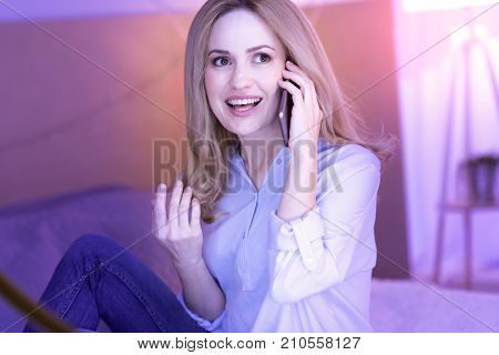 Listen to me. Lovely young blond woman smiling and moving her hand while talking on the phone