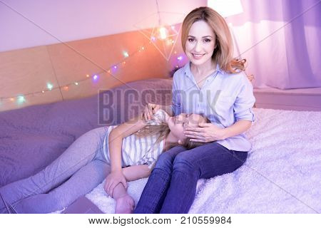 My loved daughter. Happy smiling loving mom caressing her daughter while the girl relaxing on her lap lying