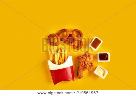 Fast food dish top view. Meat burger, potato chips and chicken. Take away composition. French fries, hamburger, mayonnaise and ketchup sauces on yellow background. Menu or receipt background