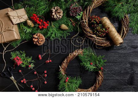 Make a Christmas wreath with your own hands. Spruce branch, Christmas wreath and gifts on a black wooden background. Workplace for preparing handmade decorations.
